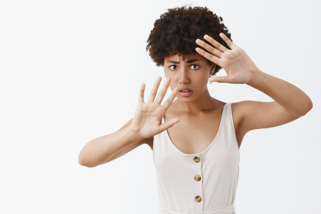 Mulher tímida se tornando vítima de machismo, com medo ,cobrindo o rosto, protegendo-se com as palmas das mãos levantadas.